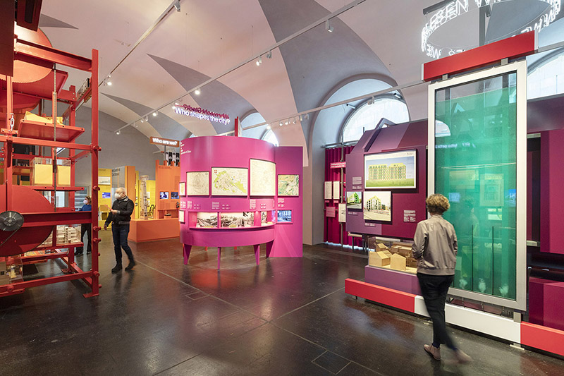 Besucher erkunden eine Ausstellung zur Stadtplanung in einem modernen Museum.
