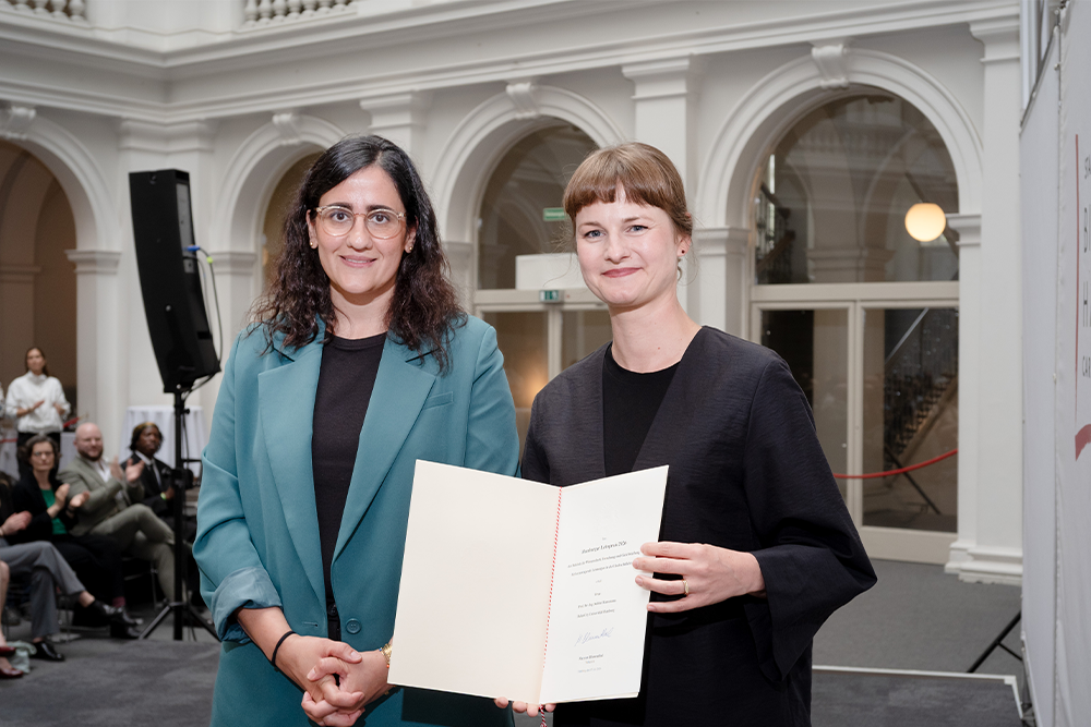 Zwei Frauen halten gemeinsam eine Urkunde bei einer Preisverleihung.